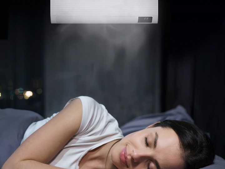 MTF Shop Samsung Klimaanlage Wärmepumpe Österreich | Eine Frau schläft entspannt unter einer Samsung WindFree Wandgerät-Klimaanlage, die kühle Luft sanft und ohne direkten Luftzug im dunkel gehaltenen Schlafzimmer verteilt.