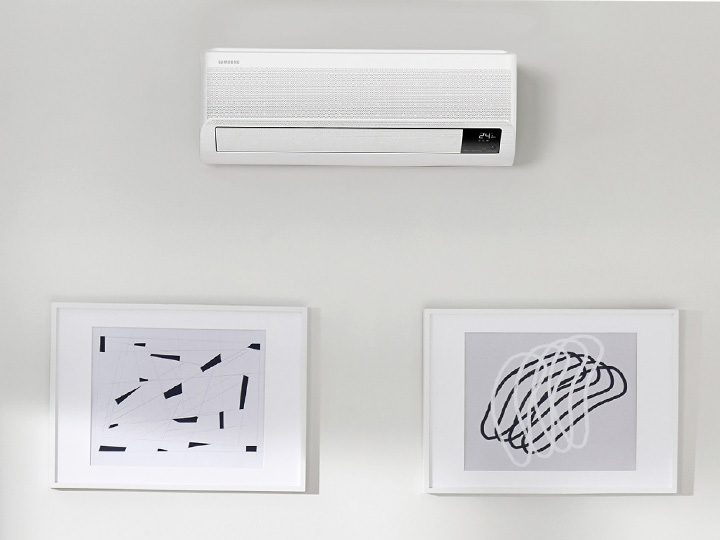 MTF Shop Samsung Klimaanlage Wärmepumpe Österreich | Eine weiße Samsung WindFree Wandgerät-Klimaanlage mit digitaler Temperaturanzeige fügt sich elegant in ein modernes Interieur über zwei minimalistischen Wandbildern in Schwarz-Weiß ein.